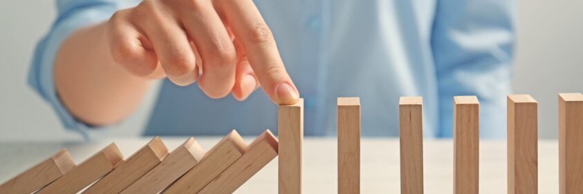 Businesswoman hand trying to stop toppling dominoes on table